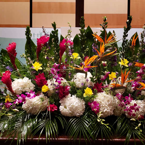 Large tropical stage arrangement with white hydrangeas, orange birds of paradise, and bright accent flowers.