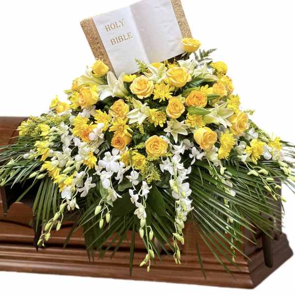 Yellow and white floral casket spray with a Holy Bible card