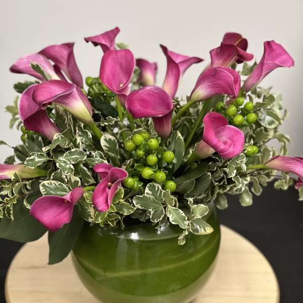 Pink calla lilies arranged in a green vase with variegated foliage