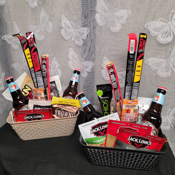 Two gift baskets filled with snacks and bottled drinks on a table