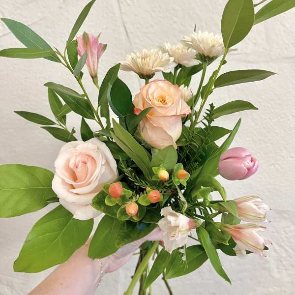 Handheld bouquet of pale pink roses and alstroemeria with greenery