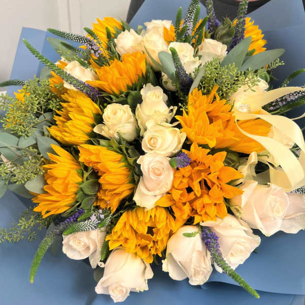 Bouquet of white roses and yellow sunflowers wrapped in blue paper