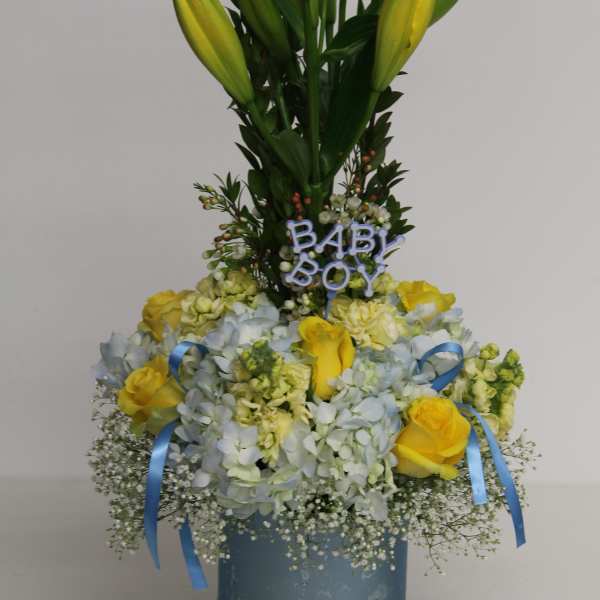 Yellow lilies and roses with blue hydrangeas in a blue vase with 'Baby Boy' pick and ribbons