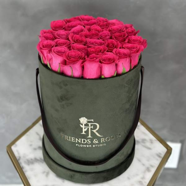 Hot pink roses arranged in a round green hat box