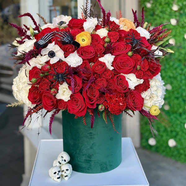Large red and white rose arrangement in a green velvet box with small skull decorations