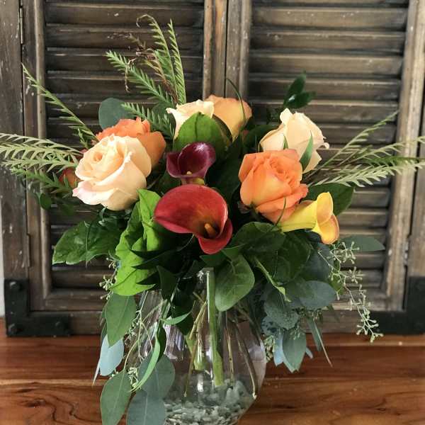 Vase arrangement of peach roses and red and yellow calla lilies in a clear glass vase