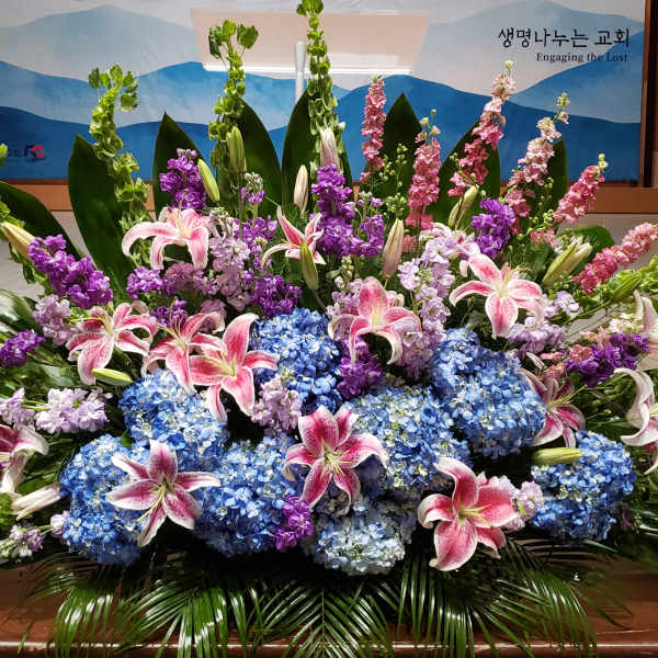 Large floral arrangement with pink lilies, blue hydrangeas, and purple flowers