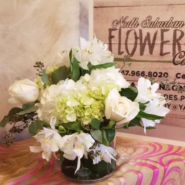 White roses and lilies arranged in a glass vase with pale green hydrangea.