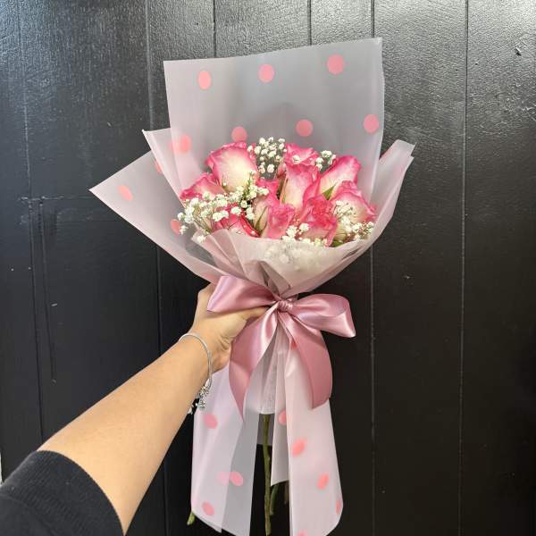 Pink rose bouquet wrapped in translucent polka-dot paper with a satin ribbon