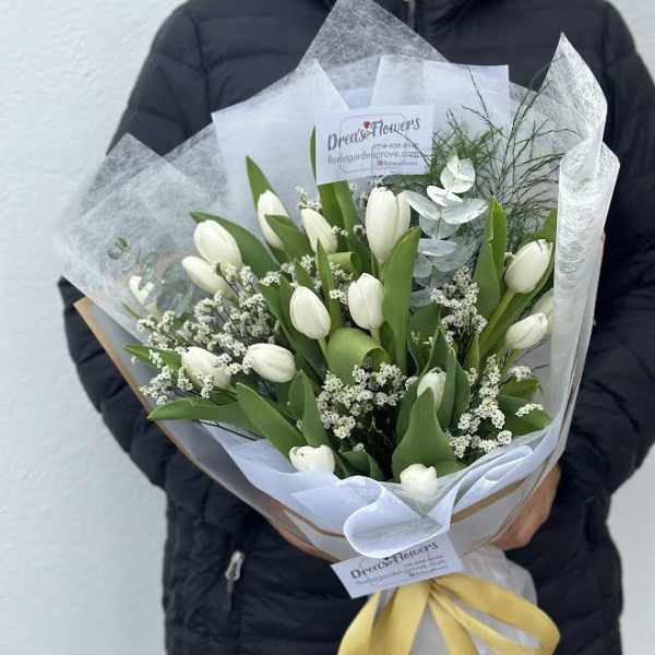 White tulips arranged in a wrapped bouquet with a yellow ribbon