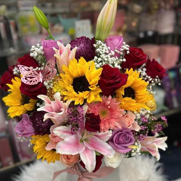Mixed bouquet of roses, sunflowers, lilies, and chrysanthemums in a white hatbox
