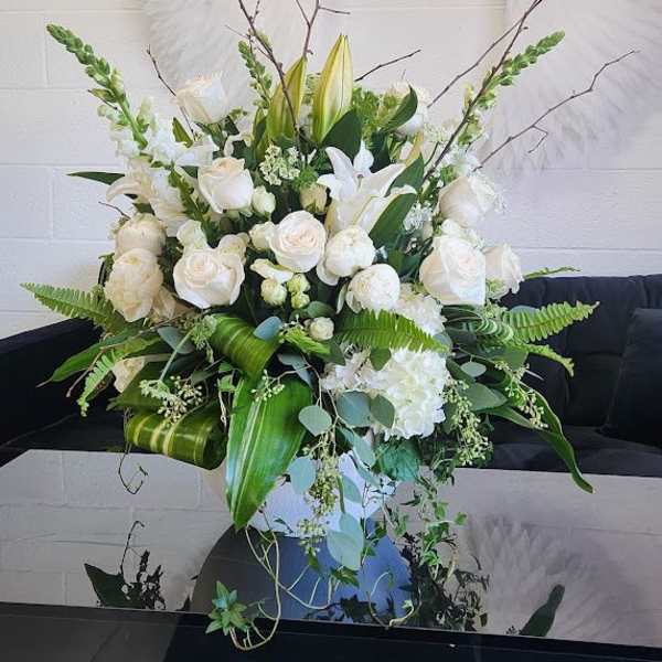Large white and green floral arrangement with roses, lilies, and snapdragons in a white vase