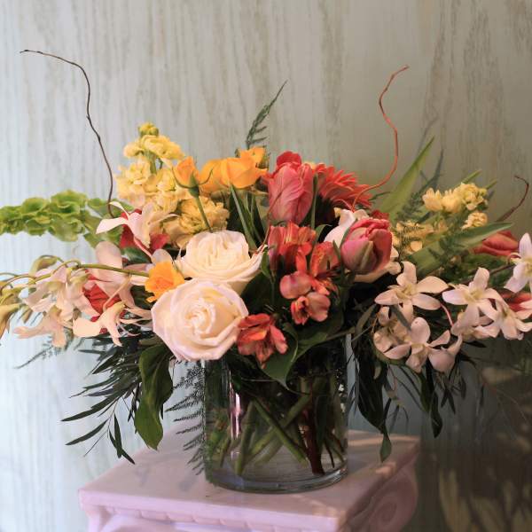 Mixed bouquet of roses, orchids, and lilies in a glass vase
