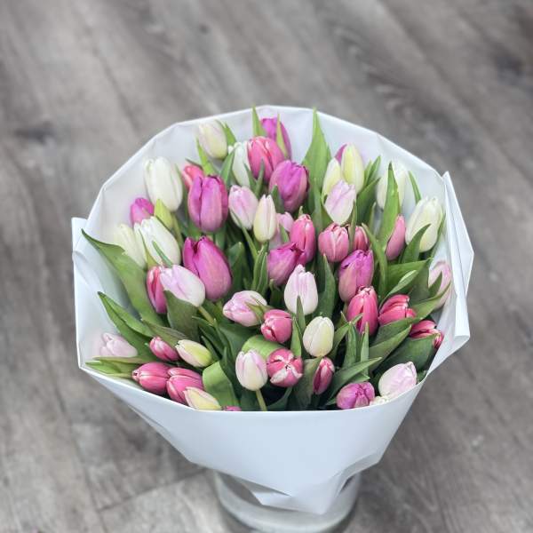 Bouquet of pink and white tulips wrapped in white paper and displayed in a clear glass vase
