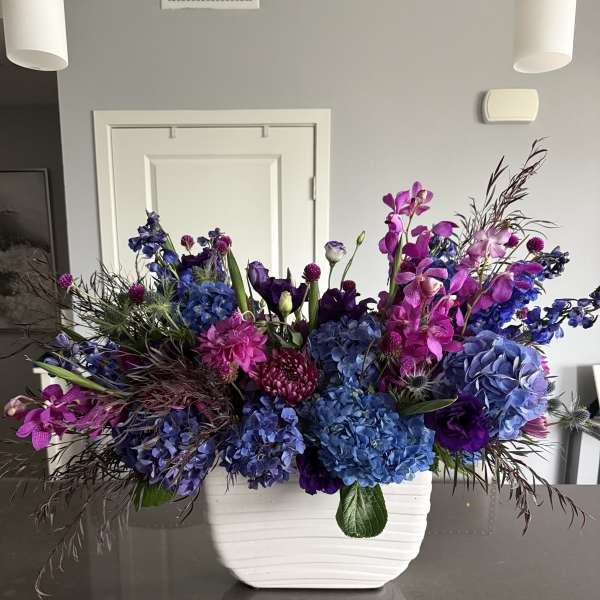 Large blue and purple floral arrangement in a white vase