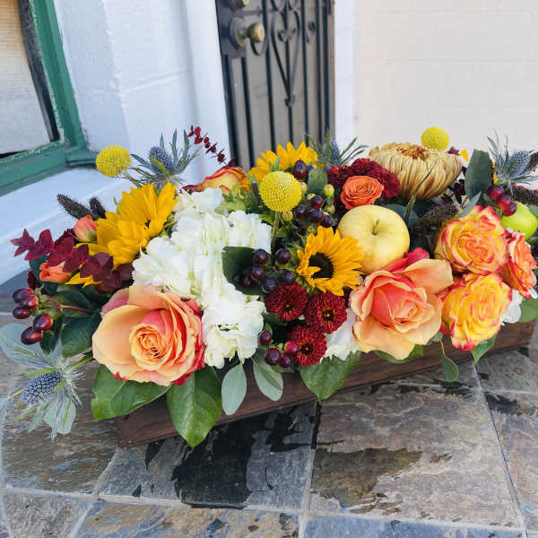 Low floral centerpiece with orange roses, sunflowers, and white blooms in a wooden box