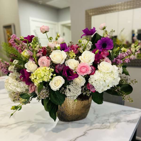 Mixed bouquet of pink, white, and purple flowers in a gold vase