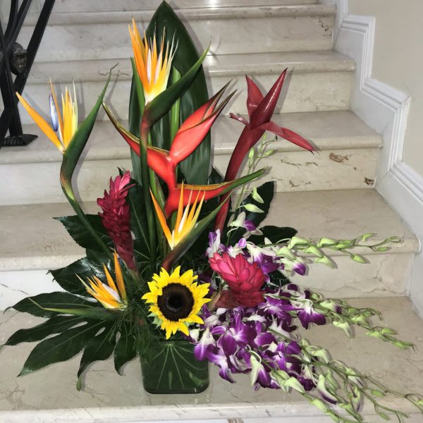 Tall tropical arrangement with birds of paradise, sunflower, and purple orchids in a green vase