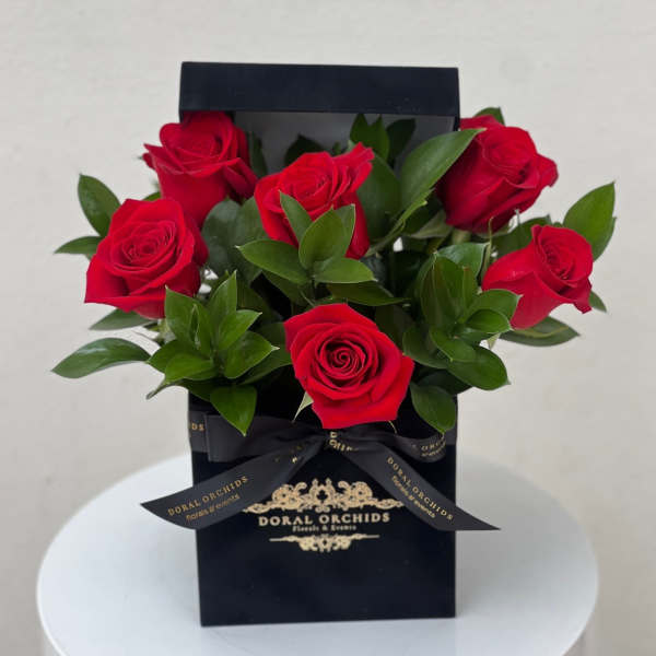 Arrangement of red roses in a black gift box with gold logo and bow