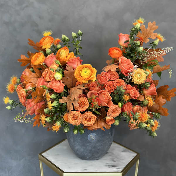 Orange and coral roses in a gray vase with autumn leaves