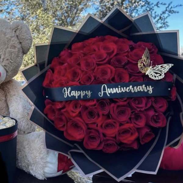 Teddy bear beside a red rose bouquet and heart-shaped chocolate box