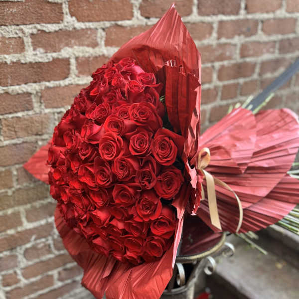 Large bouquet of tightly packed red roses wrapped in red pleated paper with ribbon
