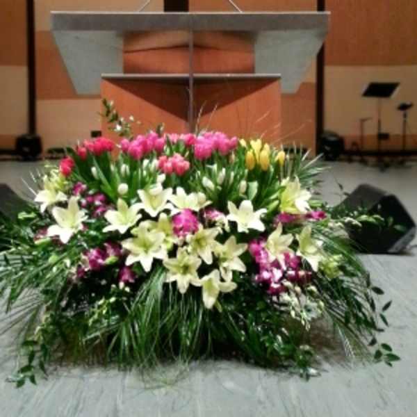 Large stage arrangement of white lilies and pink and yellow tulips set in front of a podium