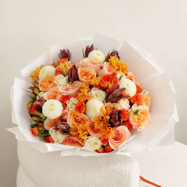 Bouquet of peach, orange, and white flowers wrapped in white paper
