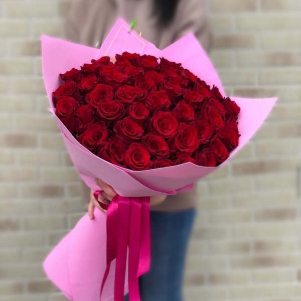 Large bouquet of red roses wrapped in pink paper with long pink ribbons