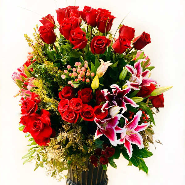 Tall arrangement of red roses and pink lilies in a dark pedestal vase