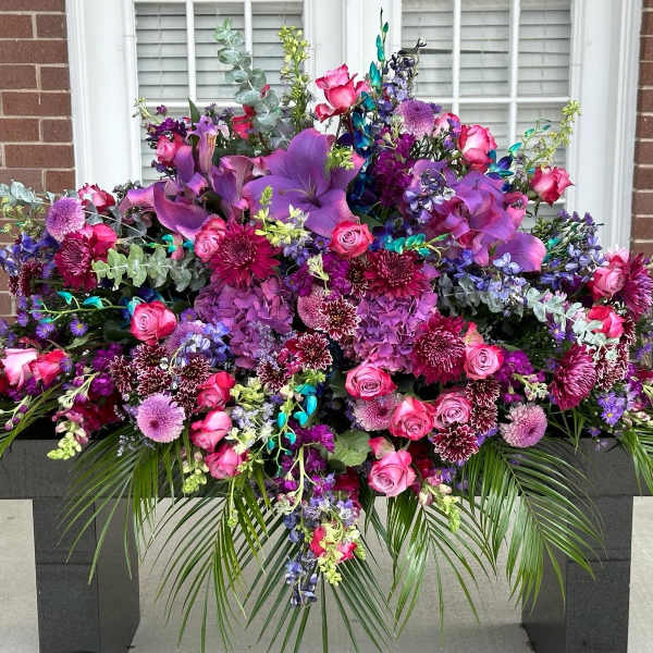 Large purple and pink floral arrangement with roses and lilies on a pedestal