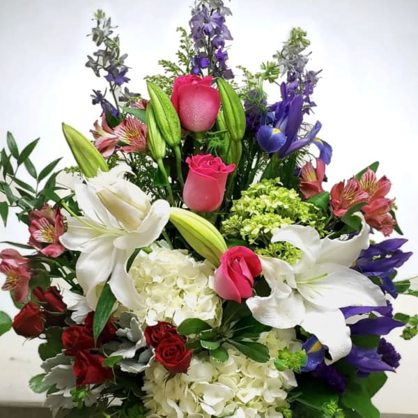 Tall mixed bouquet with white lilies, pink roses, and purple flowers in a glass vase