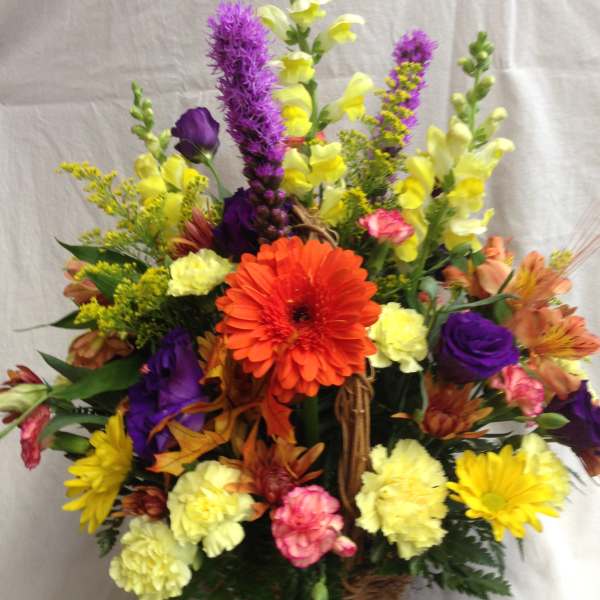 Mixed bouquet in a wicker basket with orange, purple, yellow, and pink flowers