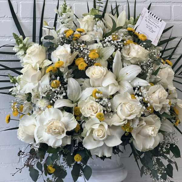 White roses and lilies in a white pedestal vase with yellow accents