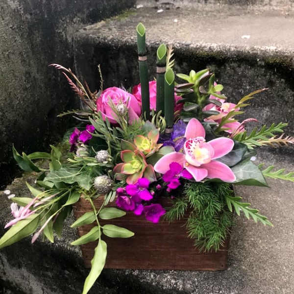 Tropical floral arrangement with pink orchids and succulents in a wooden box