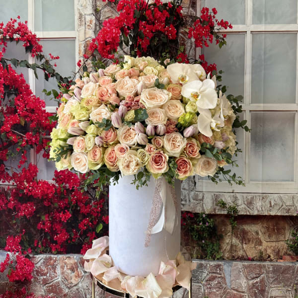Large pastel rose arrangement with white orchids in a tall white vase