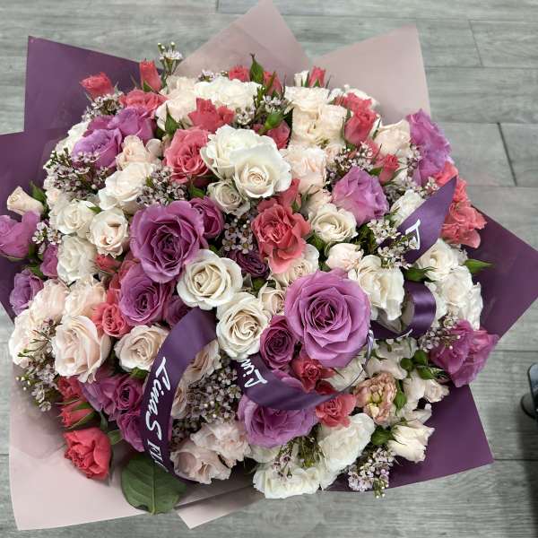Large bouquet of pink, purple, and white roses wrapped in purple paper