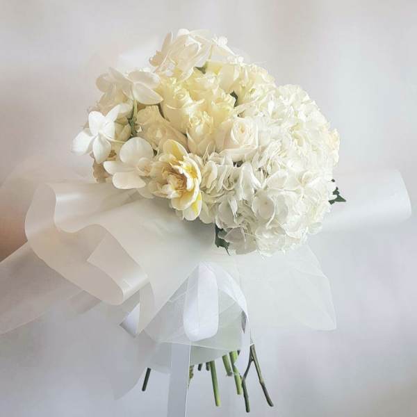 White bridal bouquet with hydrangeas and orchids wrapped in ribbon