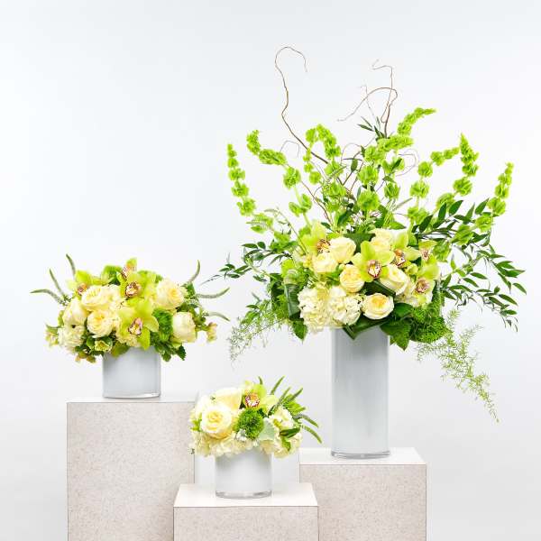 Three pale yellow floral arrangements in silver vases on pedestals
