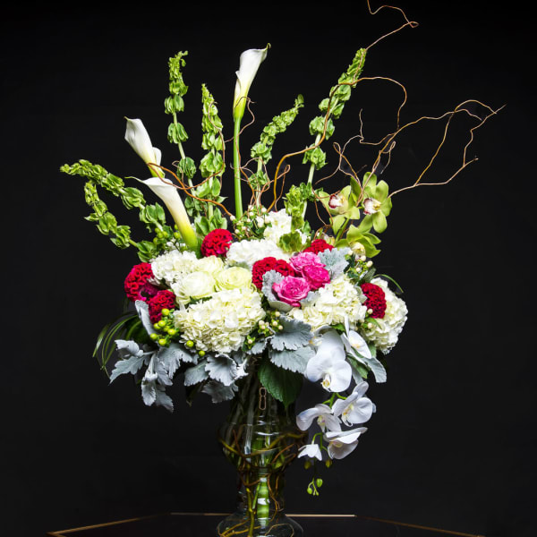 Tall floral arrangement in a glass vase with white calla lilies and orchids