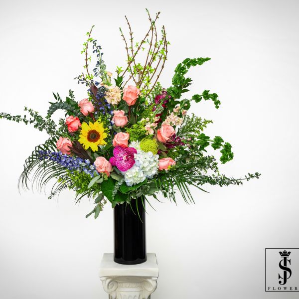 Tall mixed flower arrangement in a black vase with pink roses and a sunflower