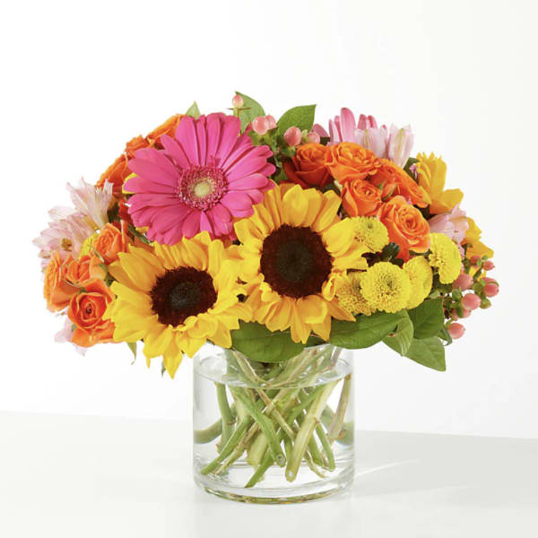 Bright mixed bouquet with sunflowers, gerbera daisies, and orange roses in a glass vase