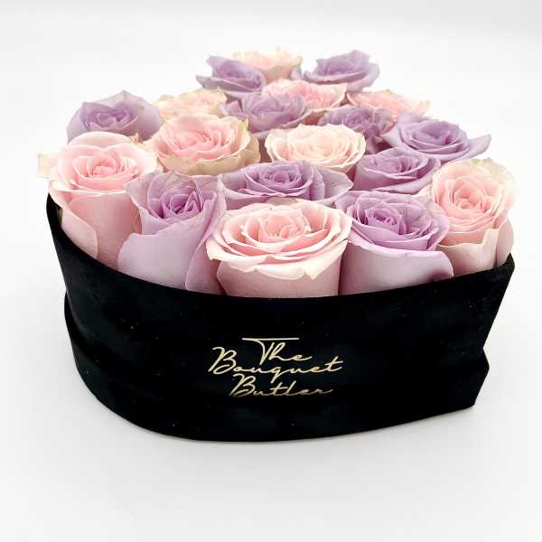 Pink and lavender roses arranged in a black hat box