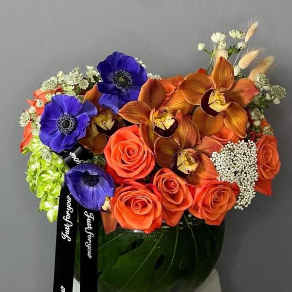 Orange roses and blue anemones in a glass vase with black ribbons