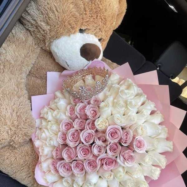 Teddy bear holding a bouquet of pink and white roses with a crown
