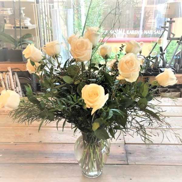 Cream roses arranged in a clear glass vase with airy greenery.