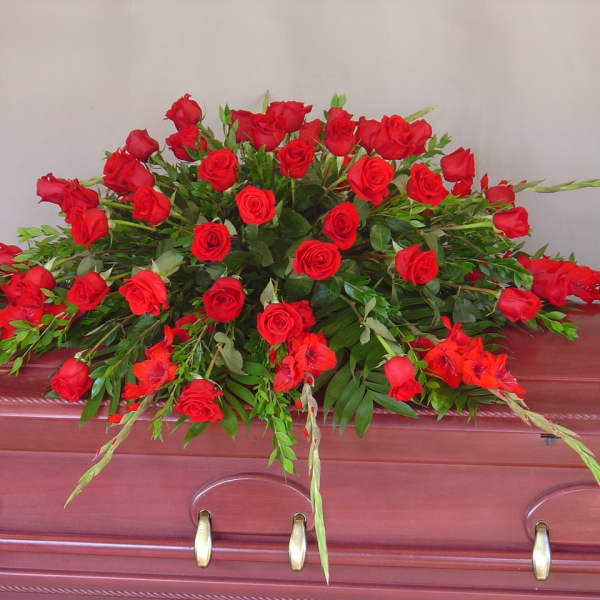 Red rose casket spray with greenery on a burgundy casket