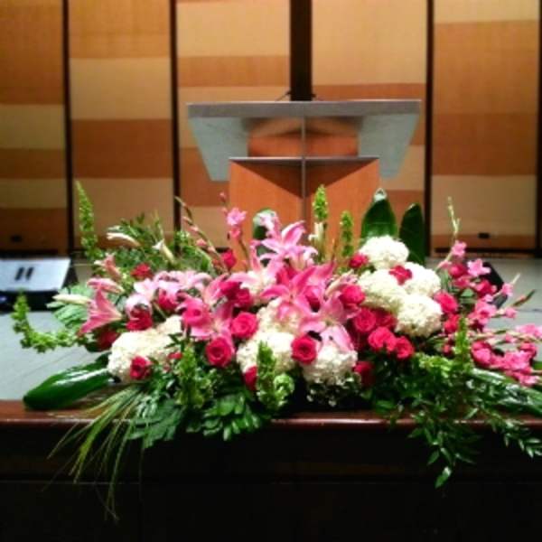 Low altar floral arrangement with pink lilies, red roses, and white blooms in front of a podium