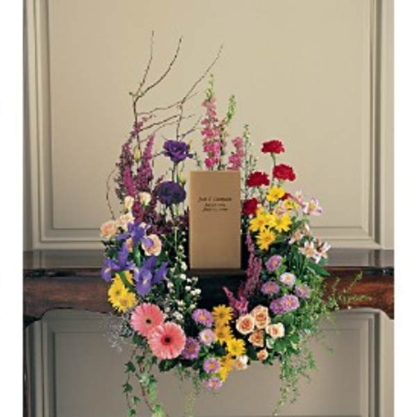Colorful mixed flower wreath with central memorial card displayed on a wooden surface