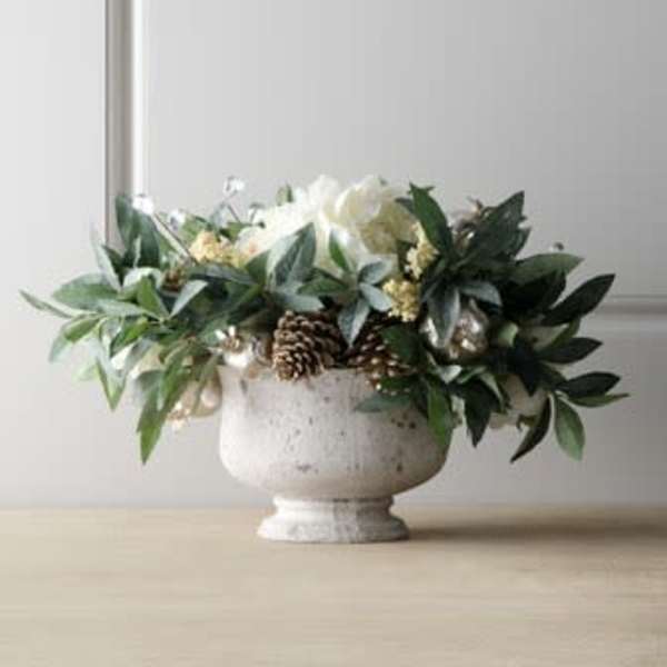 White floral arrangement in a pedestal urn with greenery and pinecones